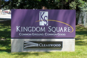 Kingdom Square Sign with Clearwood Branding A purple sign for Kingdom Square featuring the tagline "Common Ground. Common Good." with a Clearwood logo beneath it, mounted on a concrete base.
