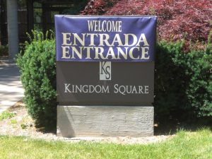 Kingdom Square Entrance Sign A sign welcoming visitors to Kingdom Square with the words "Entrada Entrance" displayed in gold lettering on a purple background.