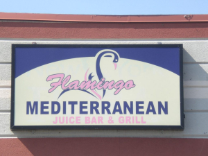 Flamingo Mediterranean Juice Bar & Grill Sign A restaurant sign for Flamingo Mediterranean Juice Bar & Grill featuring a stylized flamingo logo with bold pink and blue lettering mounted on a building exterior.