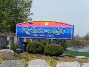 Reflection Lake Condominiums Entrance Sign A colorful entrance sign for Reflection Lake Condominiums featuring a sunset over a lake with birds flying, surrounded by landscaped greenery and rocks.
