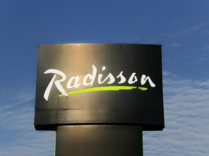 Radisson Hotel Sign A large, black Radisson hotel sign with the brand's signature white script logo and a green underline, set against a blue sky with scattered clouds.