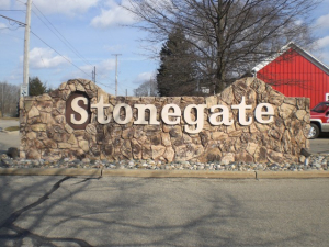 Stonegate Entrance Sign A stone entrance sign displaying the name "Stonegate" in bold, white letters, set against a rustic rock wall with a landscaped border of decorative stones.