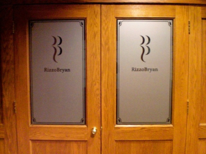 RizzoBryan Office Entrance Doors A set of wooden office doors featuring frosted glass panels with the RizzoBryan logo and name, framed by decorative corner accents.