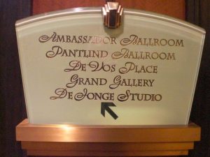 Event Venue Directional Sign A decorative directional sign with an elegant glass and bronze design, pointing to various event spaces including Ambassador Ballroom, Pantlind Ballroom, DeVos Place, Grand Gallery, and DeJonge Studio.